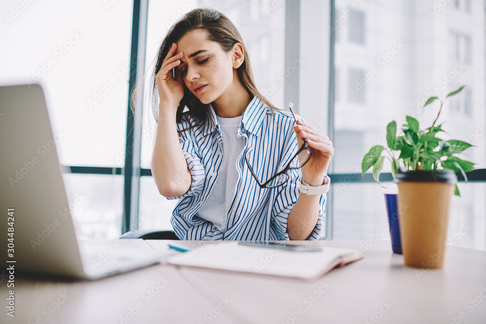 Tired female student feeling pain doing coursework project at coworking space , young female freelancer stressed about deadlines touching head disapointed with problem during working process in office Tired female student feeling pain doing coursework project at coworking space , young female freelancer stressed about deadlines touching head disapointed with problem during working process in office