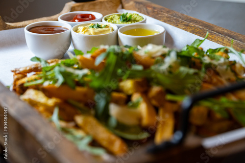 A wooden tray full of fresh fries with rocket salad, parmesan cheese and various dips
