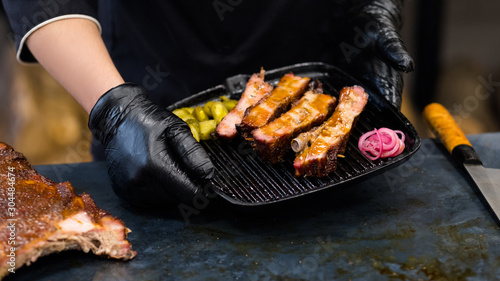 Grill restaurant kitchen. Cropped shot of chef in black cooking gloves holding smoked pork ribs in griddle pan. photo