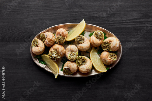 top view of delicious cooked escargots with lemon on black wooden table