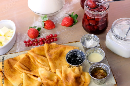 Traditional russian pancakes, blini. Served with jams, sour cream, milk and strawberry on the plate. Side view photo