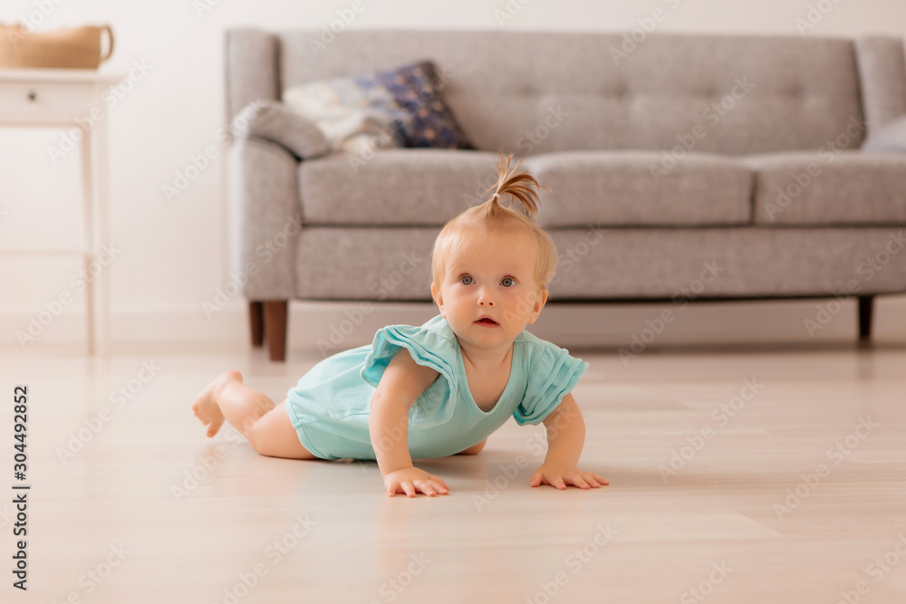 healthy baby girl in a blue bodysuit in a room next to a gray sofa is learning to walk. the comfort of the home. the child smiles healthy baby girl in a blue bodysuit in a room next to a gray sofa is learning to walk. the comfort of the home. the child smiles