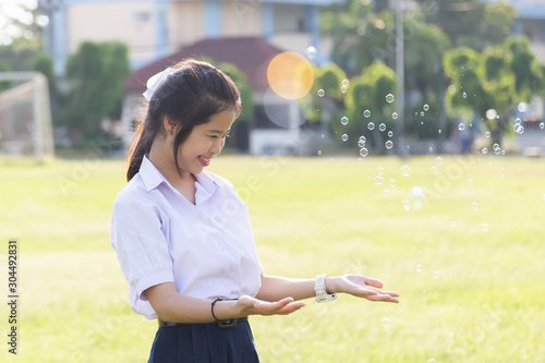 Asian cute girl in a white school uniform is playing a bubble balloon on the lawn. Cute girl is playing soap bubbles in the garden.