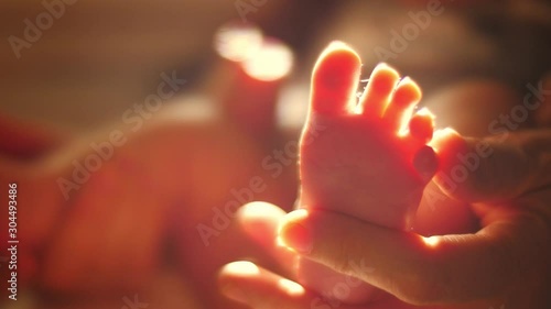 Mother's hand holding newborn baby foot in sunlight. Closeup, shallow DOF. 4K UHD.