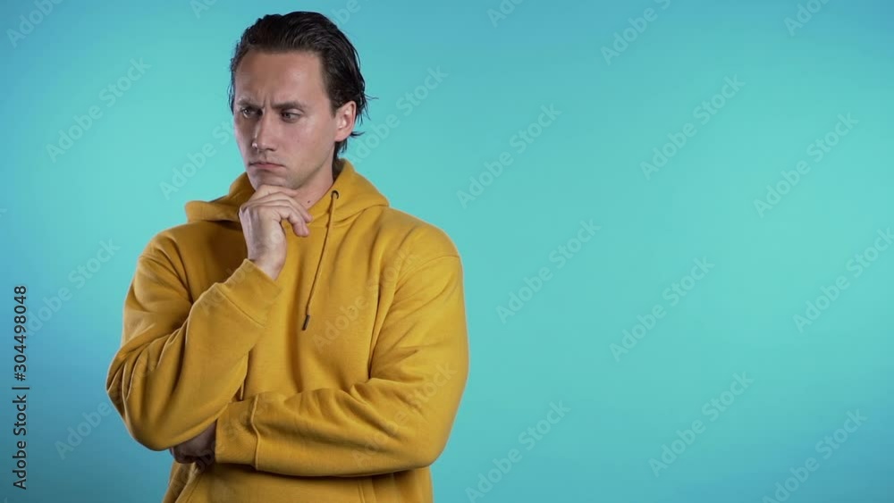 Copy space.Thinking man looking up and around on blue background. Worried contemplative face expressions. Handsome male model in yellow hoodie. Copy space.Thinking man looking up and around on blue background. Worried contemplative face expressions. Handsome male model in yellow hoodie.