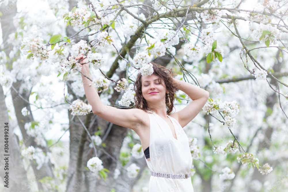 A portrait of beautiful young Caucasian woman with curly dark hair in blossoming orchard	