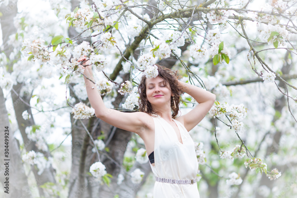 A portrait of beautiful young Caucasian woman with curly dark hair in blossoming orchard A portrait of beautiful young Caucasian woman with curly dark hair in blossoming orchard