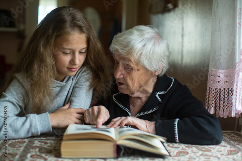 Cute teen girl with her old great-grandmother reading a book.