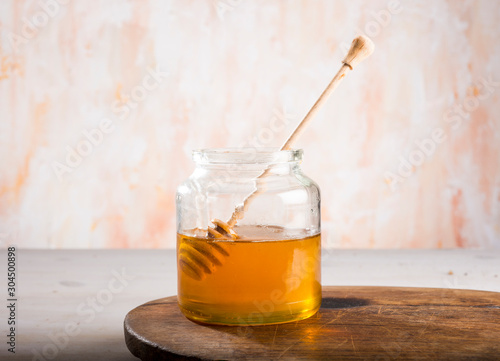 Honey and dipper in glass jar on a wooden floor