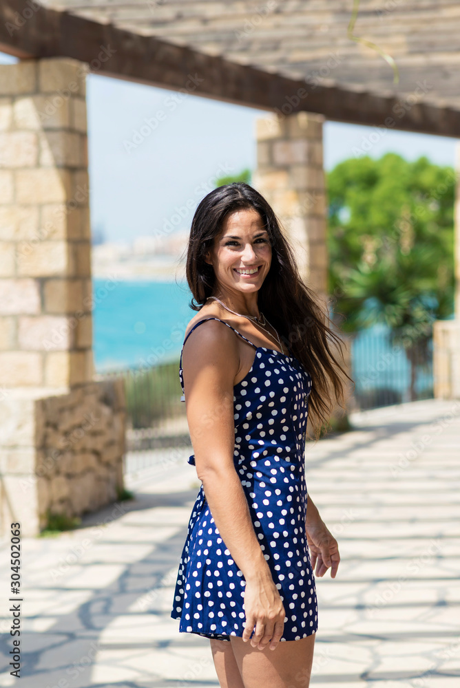 Beautiful hispanic woman in blue dress standing outdoors while looking camera