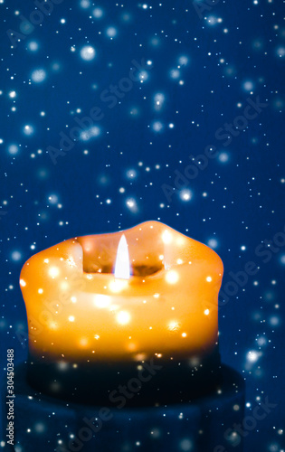 Canvas Print Yellow holiday candle on blue sparkling snowing background, luxury branding desi