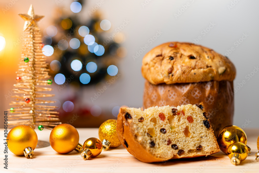 Delicious Panettone slice with candied fruits with blinking blurred christmas lights. Dry fruits. Christmas ornaments and decoration tree.