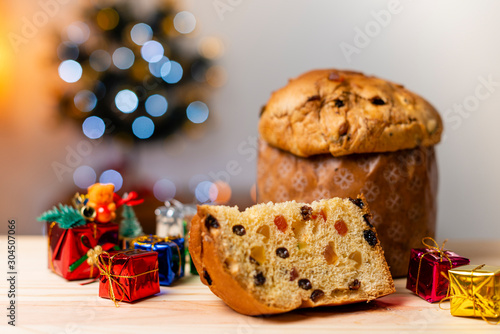 Delicious Panettone slice with candied fruits with blinking blurred christmas lights. Dry fruits. Ornament and tree gifts.