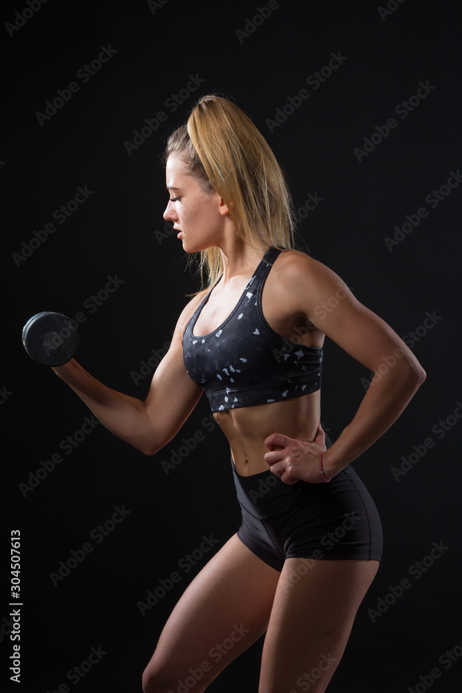 Fototapeta premium beautiful young woman with an athletic figure on a black background goes in for sports with dumbbell