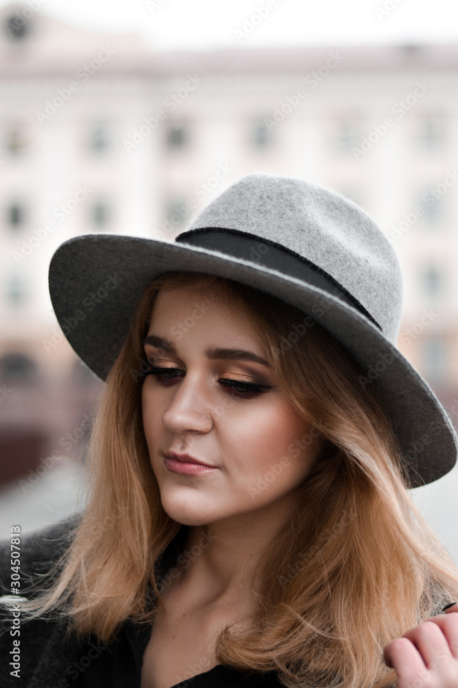 Portrait of beautiful woman with blond hair wearing hat and gray coat. Outdoor portrait in city Portrait of beautiful woman with blond hair wearing hat and gray coat. Outdoor portrait in city