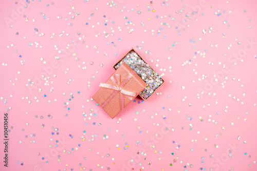 Pink open gift box with bibbon full of holographic stars confetti. Minimal flat lay photo