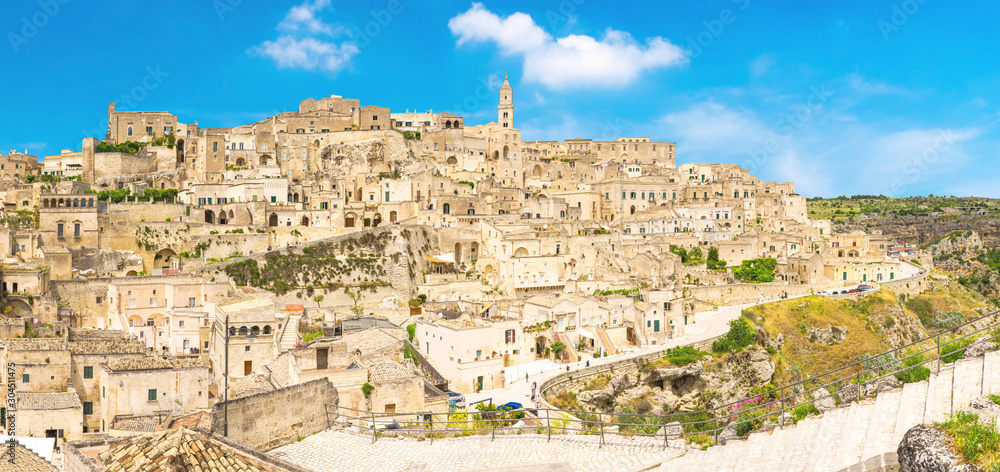 Aerial panoramic view of historical centre Sasso Caveoso of old ancient town Sassi di Matera with rock cave houses, blue sky white clouds, UNESCO World Heritage Site, Basilicata, Southern Italy
