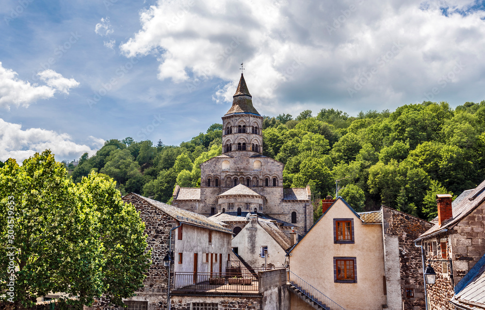 Basilica Notre Dame d’Orcival seen from the village. Parts of old houses are at foreground. Puy-de-Dome department in French Auvergne.