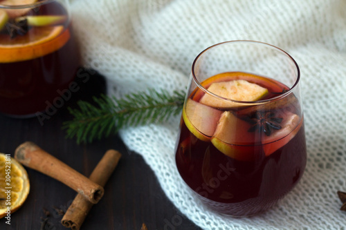 winter still life. red mulled wine in a glass with orange, apple and cinnamon, anise star and warm white knitted plaid on a dark wooden background with green pine branch. copy space