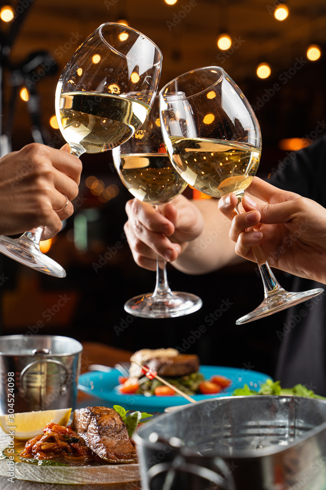 People clink glasses with white wine above a table full of meals in a restaurant