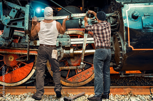 Tableau sur toile Two mechanics repair an old steam locomotive in a depot