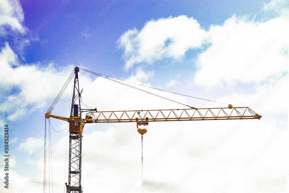 High-rise construction crane on a background of blue sky and clouds. Front view.