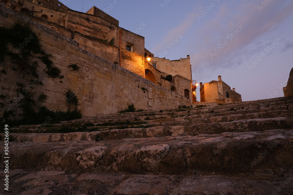 Deserted street with night light in the city of Matera in Italy. Beige tufa stone houses.