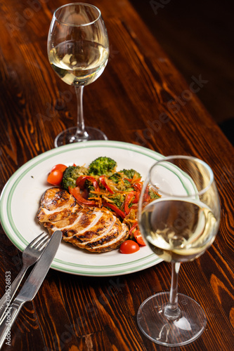Grilled and sliced chicken breast with glasses of white wine on wooden table