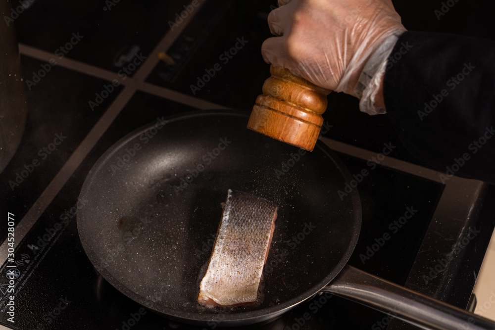 Chief is frying a piece of raw salmon on a pan in a restaurant kitchen Chief is frying a piece of raw salmon on a pan in a restaurant kitchen