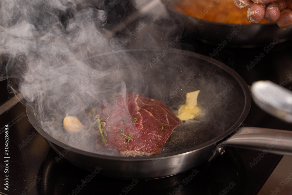 Frying a red meat steak on a pan with garlic and rosemary on a restaurant kitchen Frying a red meat steak on a pan with garlic and rosemary on a restaurant kitchen