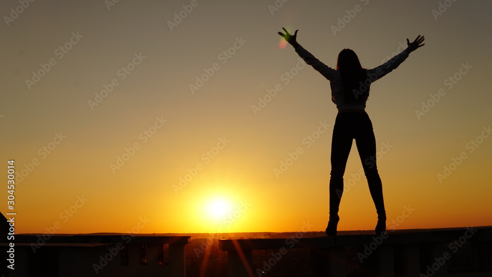 Fototapeta premium Young girl in sports uniform sits on the edge of the roof during sunset.
