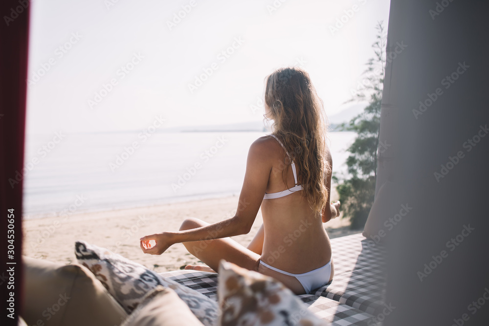 Woman in bikini meditating on beach