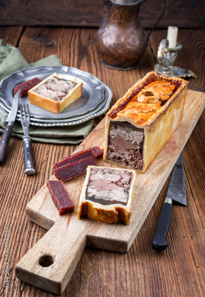 Fototapeta premium Traditional French Pate en croute with goose meat and liver ofered with quince cheese as closeup on a modern design wooden board