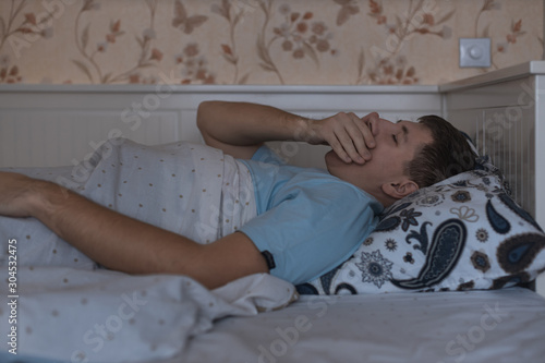 Adult sleepy yawning man covering mouth with hand awake late at night in bed, can not fall asleep/ lying in bed, sleepy tired, sleep disorder, insomnia and sleeplessness concept.