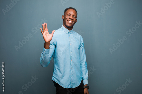 young african american black man smiling happily and cheerfully, waving hand, welcoming and greeting you, or saying goodbye photo