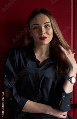 Portrait of young attractive stylish girl or model with long hair and red lips wearing black blouse. Studio shot on red background.