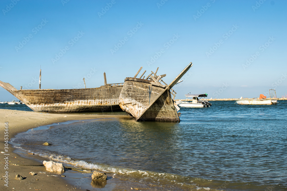 an abandoned broken old wooden boat at a beach and other speed modern boats in the background and blue sky an abandoned broken old wooden boat at a beach and other speed modern boats in the background and blue sky