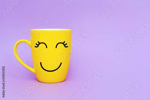 Smiley yellow coffee cup on purple background. Happy friday word concept. Minimalism style, romantic mood, good morning, happiness, break time