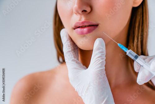 Close up of beautiful woman getiing injection in her lips on background