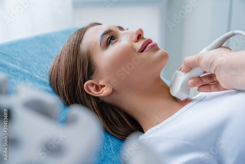 Close up shot of young woman getting her neck examined by doctor using ultrasound scanner at modern clinic photo