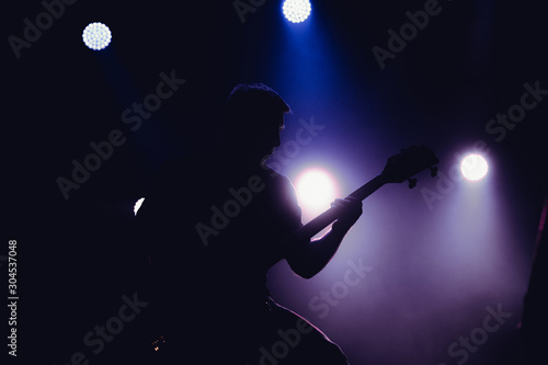 Rock band performs on stage. Guitarist plays solo. silhouette of guitar player in action on stage in front of concert crowd.