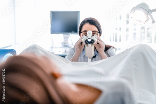 Adult woman gynecologist examining patient in hospital using colposcope photo