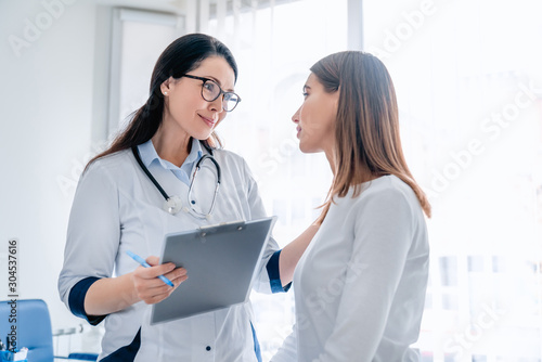 Doctor talking to female patient in working cabinet at hospital photo