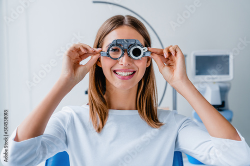 Young woman checking vision with eye test glasses during a medical examination at the ophthalmological office