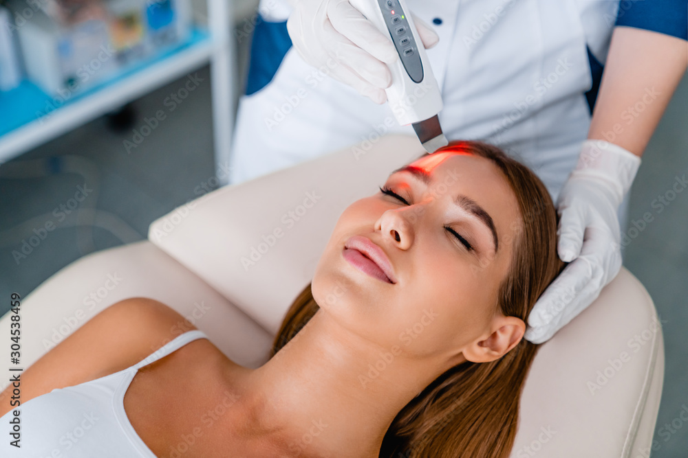 Naklejka premium Cosmetologist make face while procedure ultrasound facial peeling in cosmetology cabinet