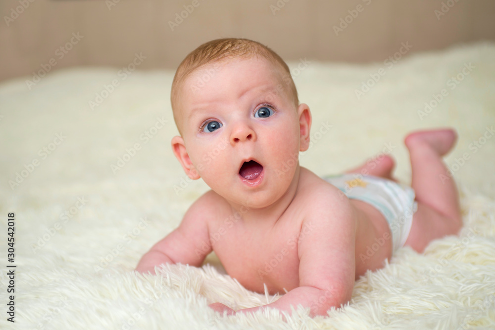 Smiling baby is looking at camera lying on a white blanket. Portrait of a beautiful smiling baby Smiling baby is looking at camera lying on a white blanket. Portrait of a beautiful smiling baby
