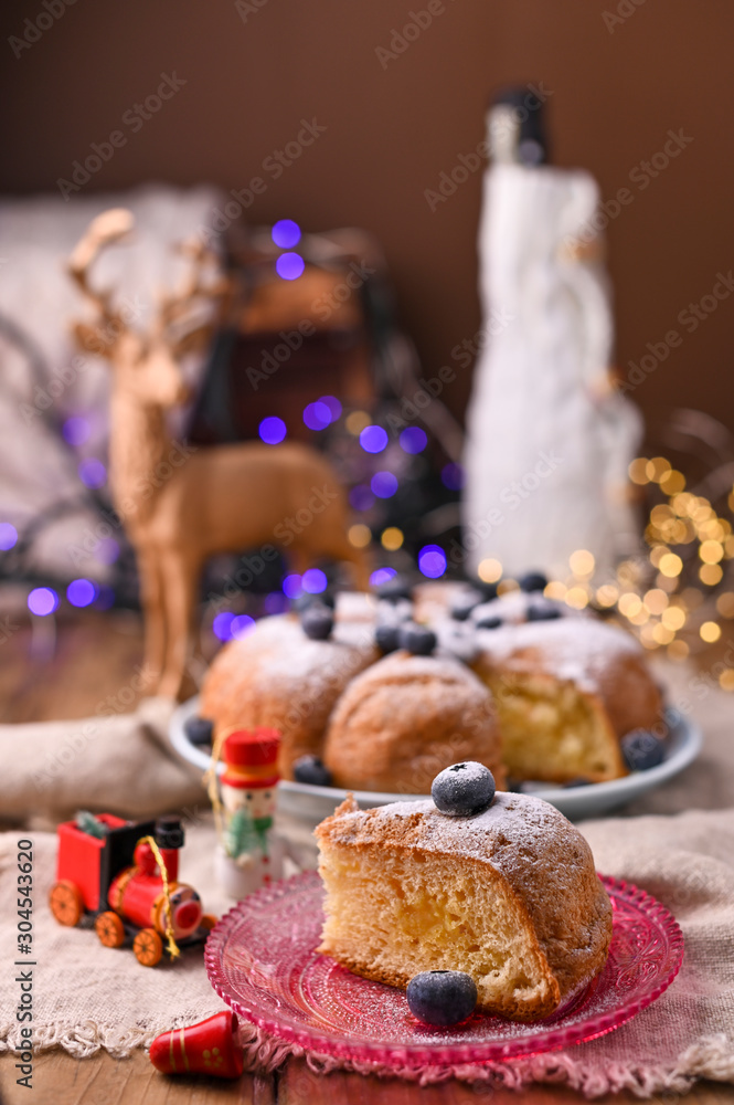 Christmas cake with berries and icing sugar on a wooden background. piece of cake. Traditional pastries in Italy. Bokeh on background