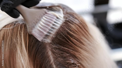 The client is in the beauty salon. The hairdresser mixed the colors. The girl is dyeing the client's hair.