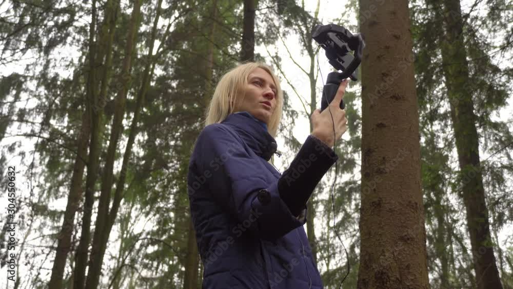 Woman blogger makes video with her phone and gimbal in the forest on nature. She cries and upset tells her viewers and followers on Instagram and YouTube. Woman blogger makes video with her phone and gimbal in the forest on nature. She cries and upset tells her viewers and followers on Instagram and YouTube.