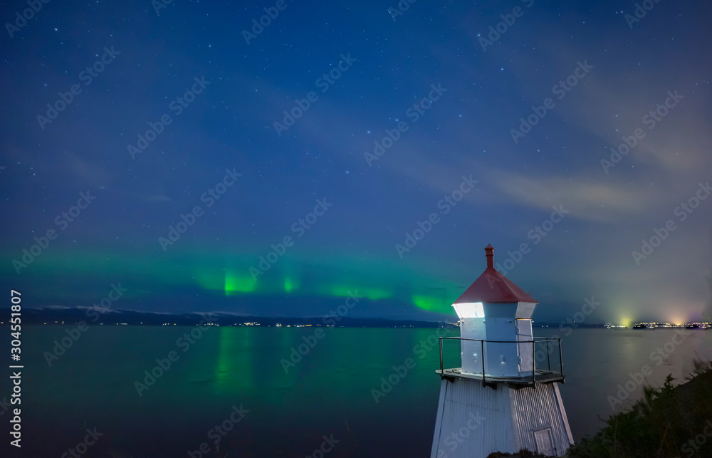 lighthouse at night with a aurora borealis in the horizon in Norway
